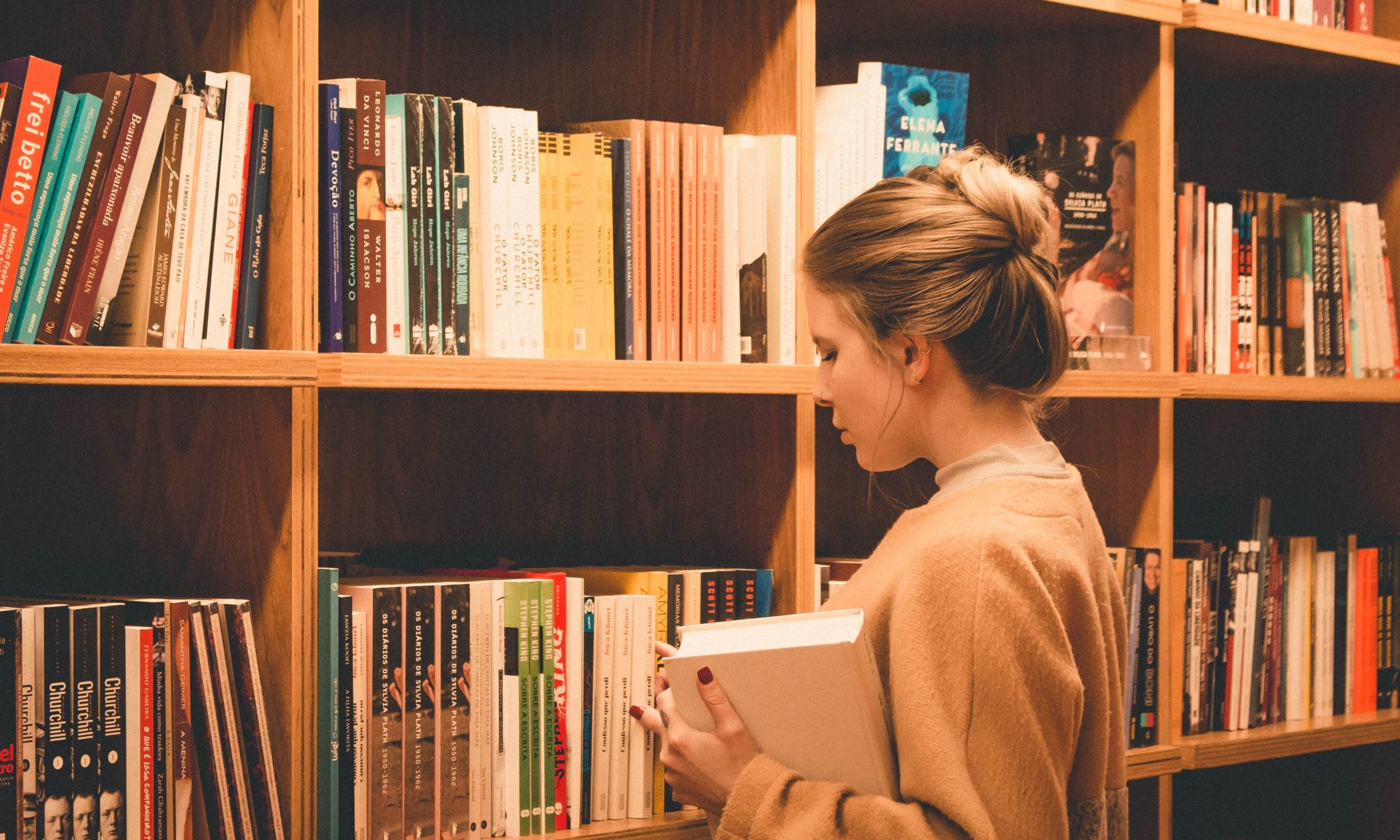 Plano fechado sobre rapariga junto de prateleira de livros, numa biblioteca